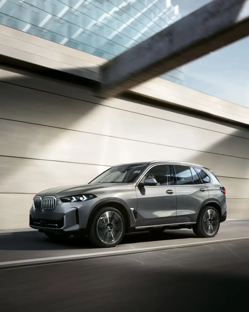 2026 BMW X5 driving past a modern building