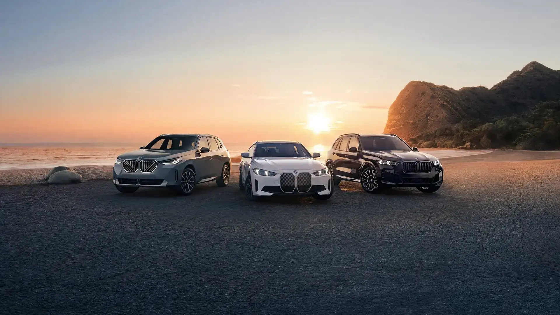 BMW X-model SUV, i4, and X5 parked at the coast at sunset