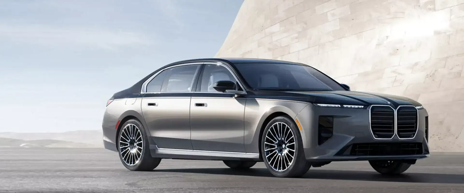 2027 BMW 7 Series luxury sedan in silver, shown from the front three-quarter angle against a minimalist concrete backdrop