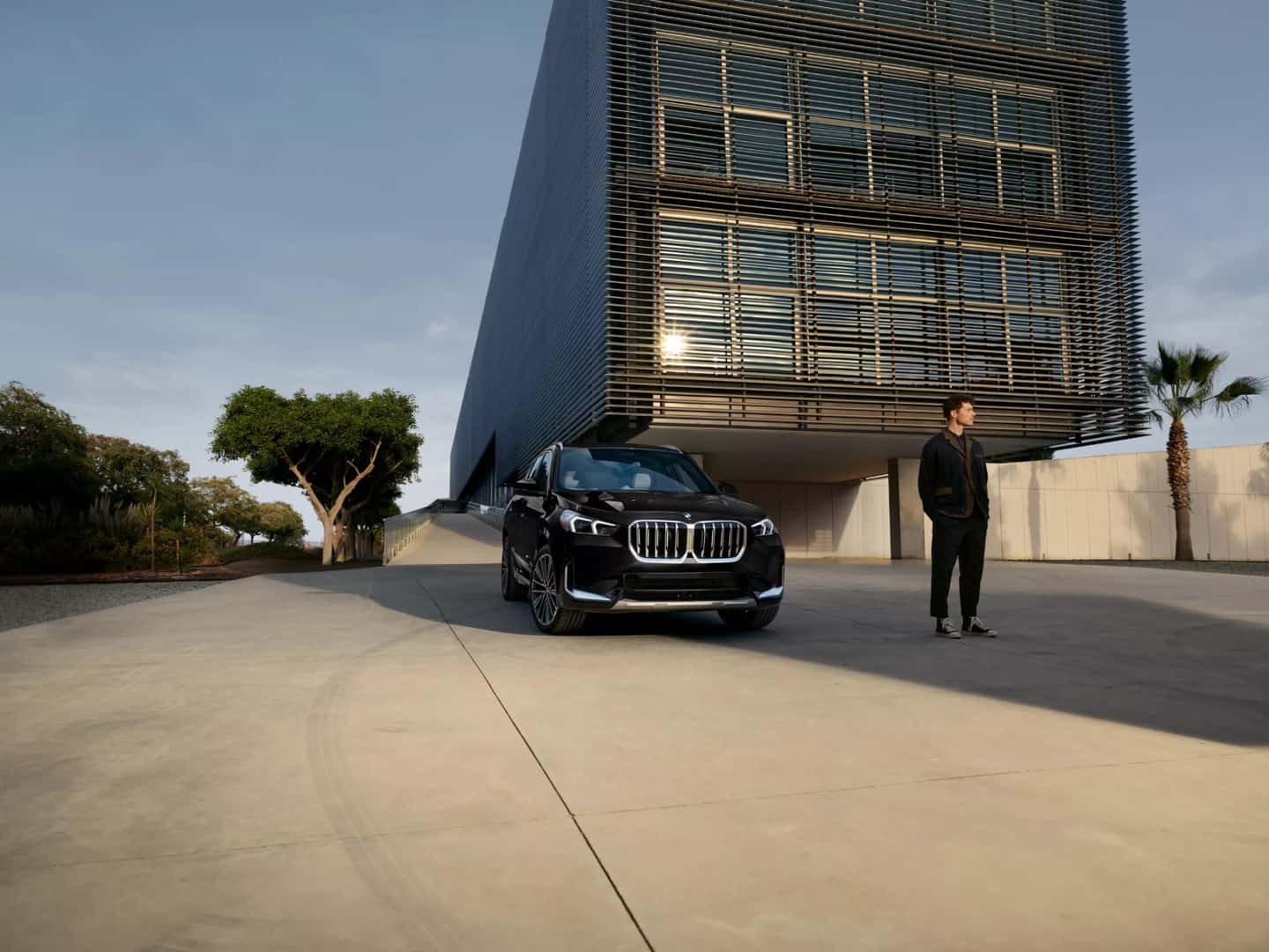 A black BMW X1 parked outside a modern building with a person beside it