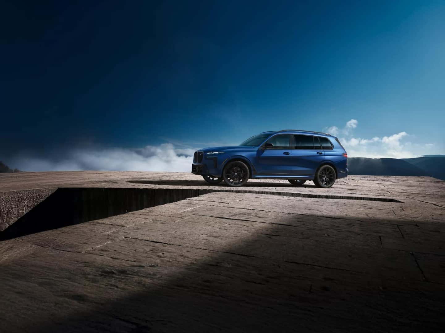 A blue BMW X7 M60i parked on a concrete ledge above the clouds