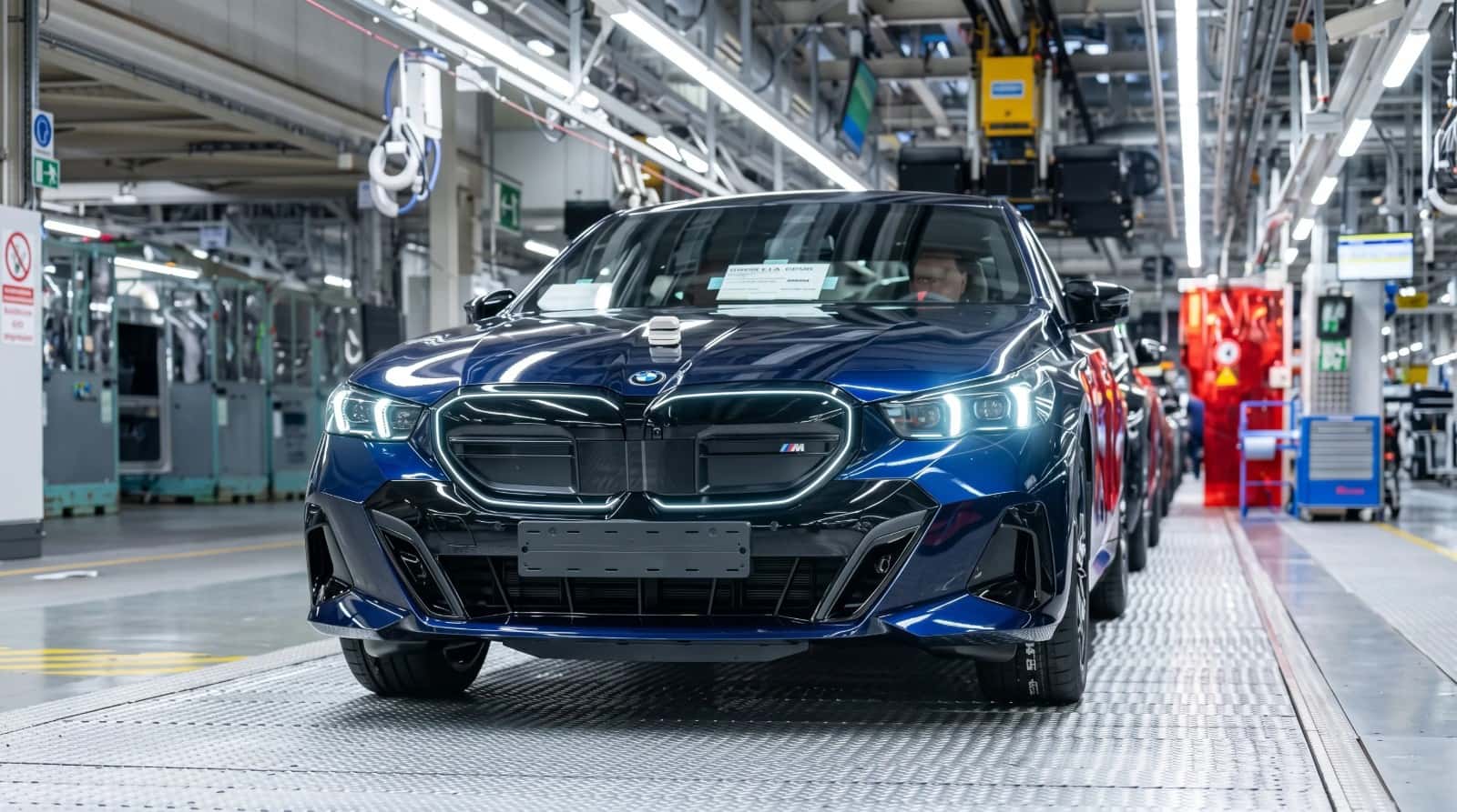 A dark blue BMW 5 Series at the end of a production line, seen head-on