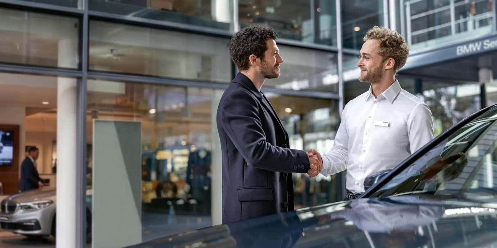 A customer and a BMW advisor shaking hands outside the showroom entrance