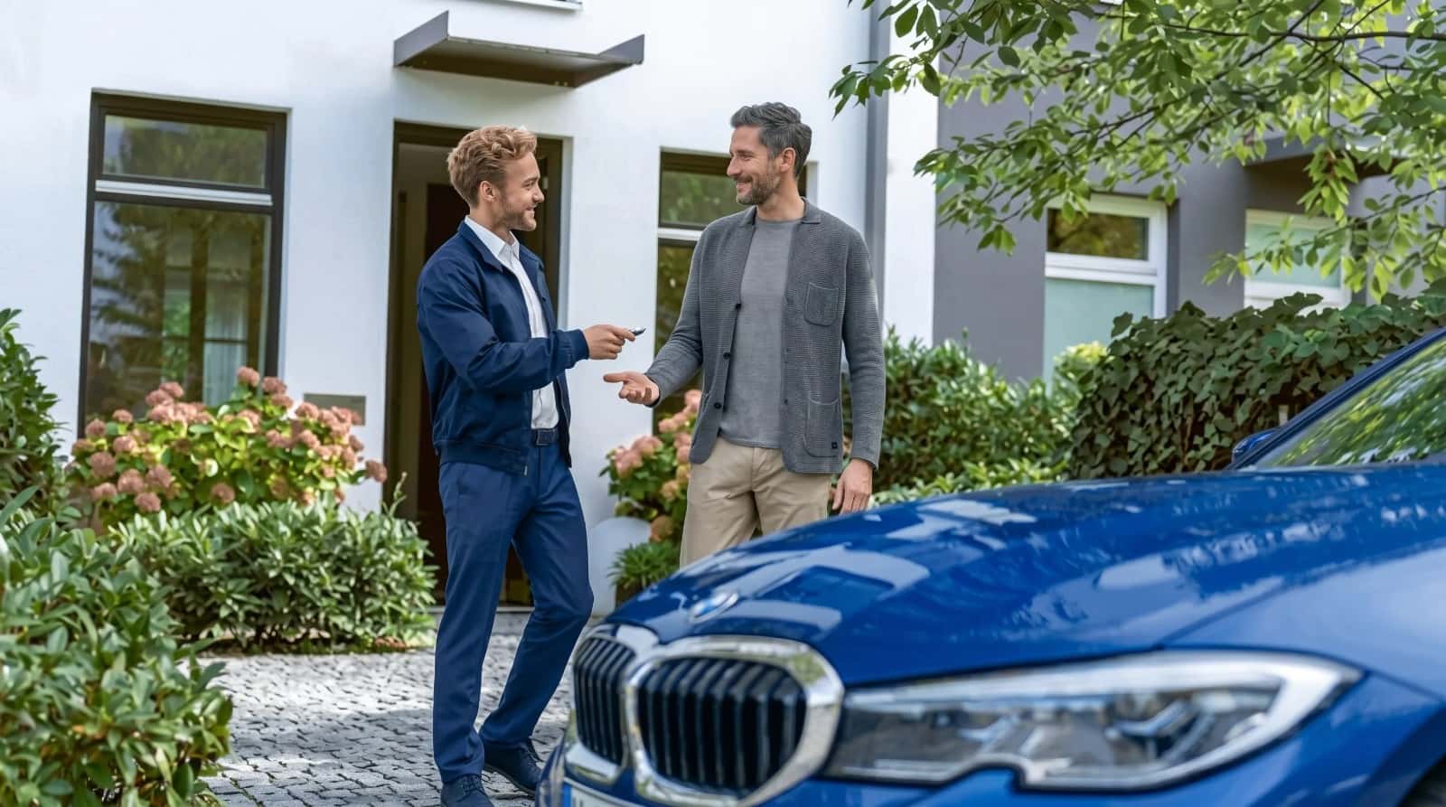A BMW advisor handing a customer the key beside a blue BMW sedan