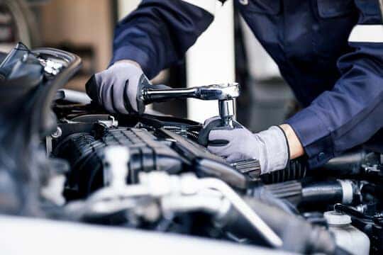 A technician in gloves working on an engine with a ratchet under an open hood