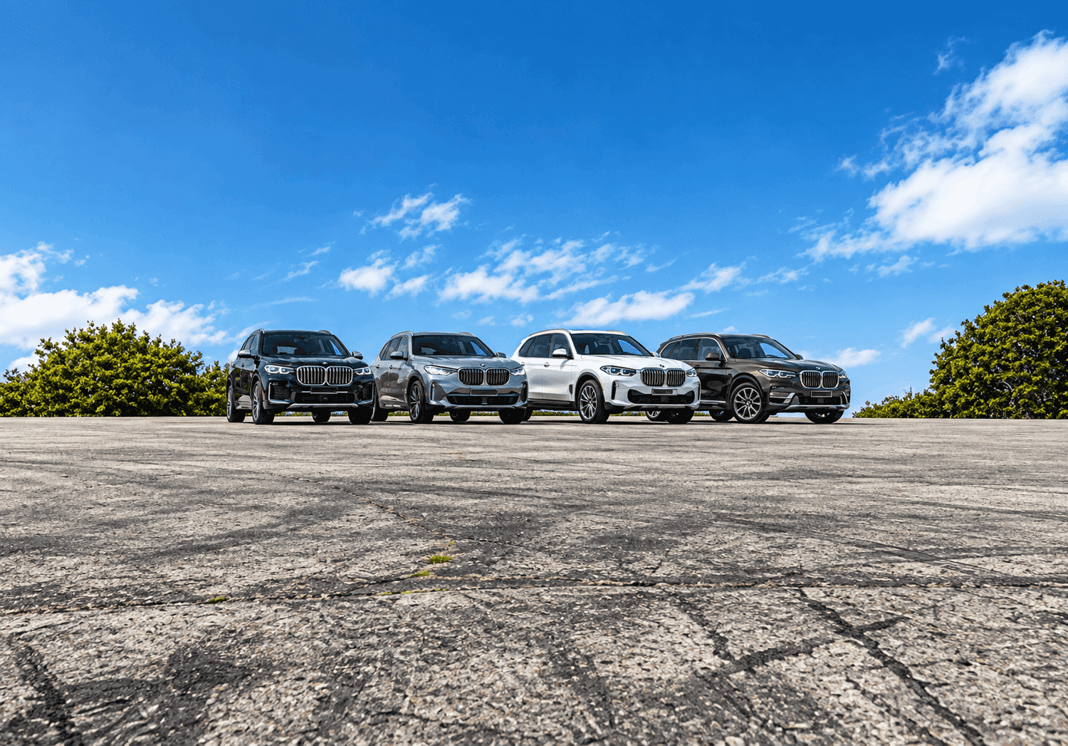 Four BMW X models lined up on concrete under a blue sky, seen head-on