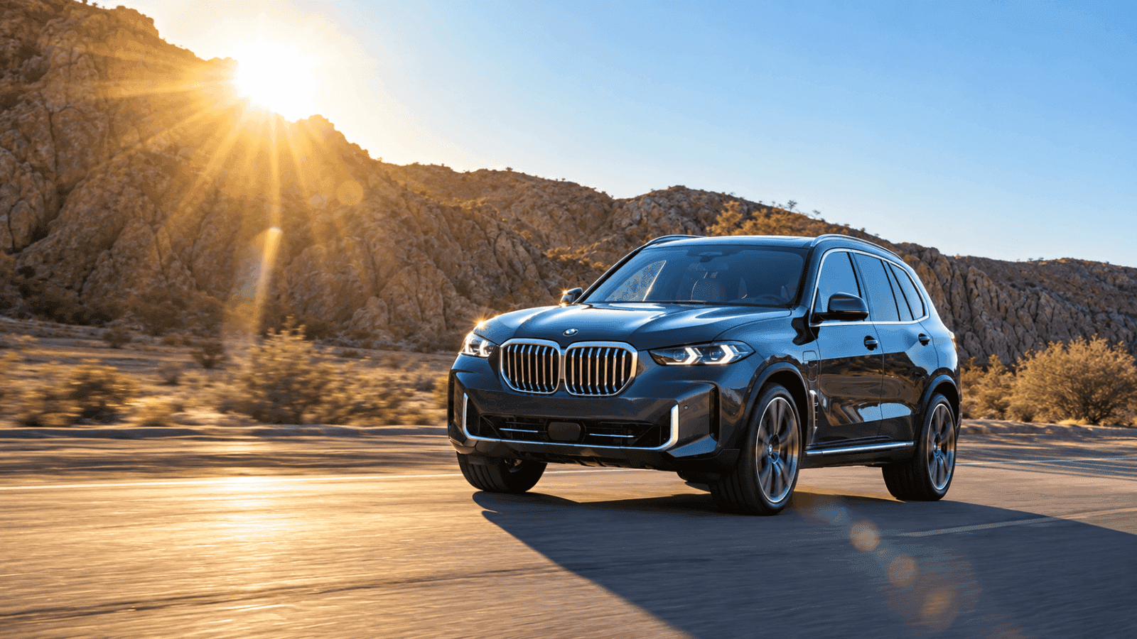 A black BMW X5 driving along a canyon road into low sun, front three-quarter view