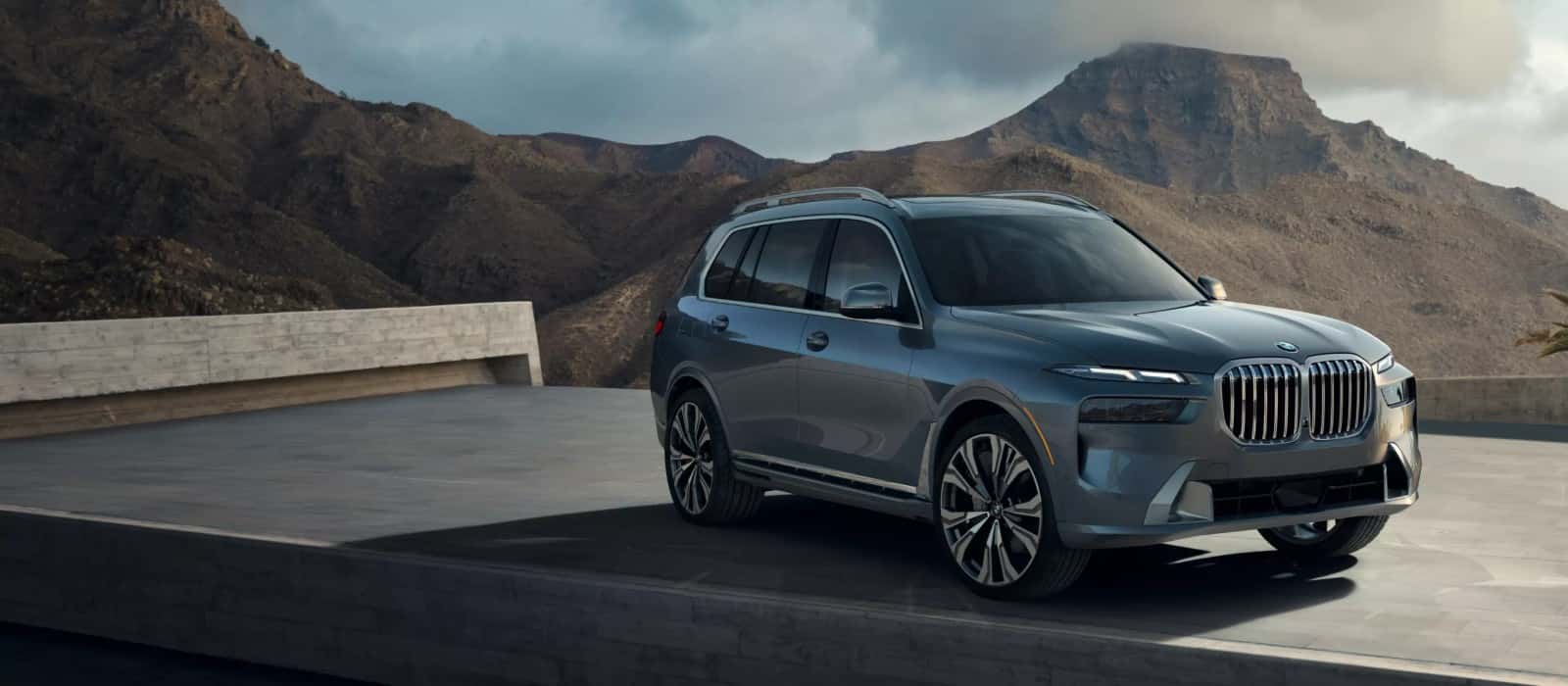 A gray BMW X7 parked on a mountain overlook, seen from the front three-quarter