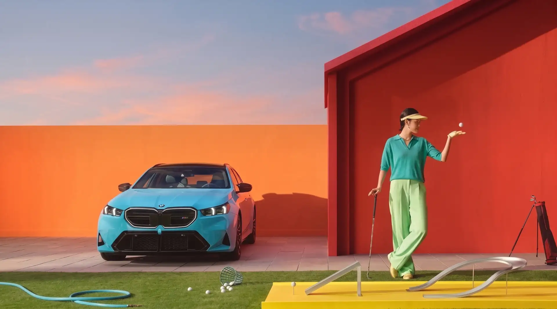 A turquoise BMW sedan parked beside a red house, with a golfer practicing on an artificial green