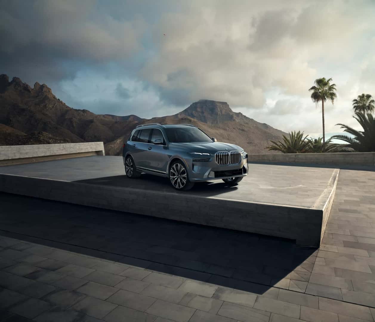 A BMW X7 parked on a stone terrace with mountains and palms behind it