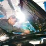 A mechanic is shown working on a car under the hood.