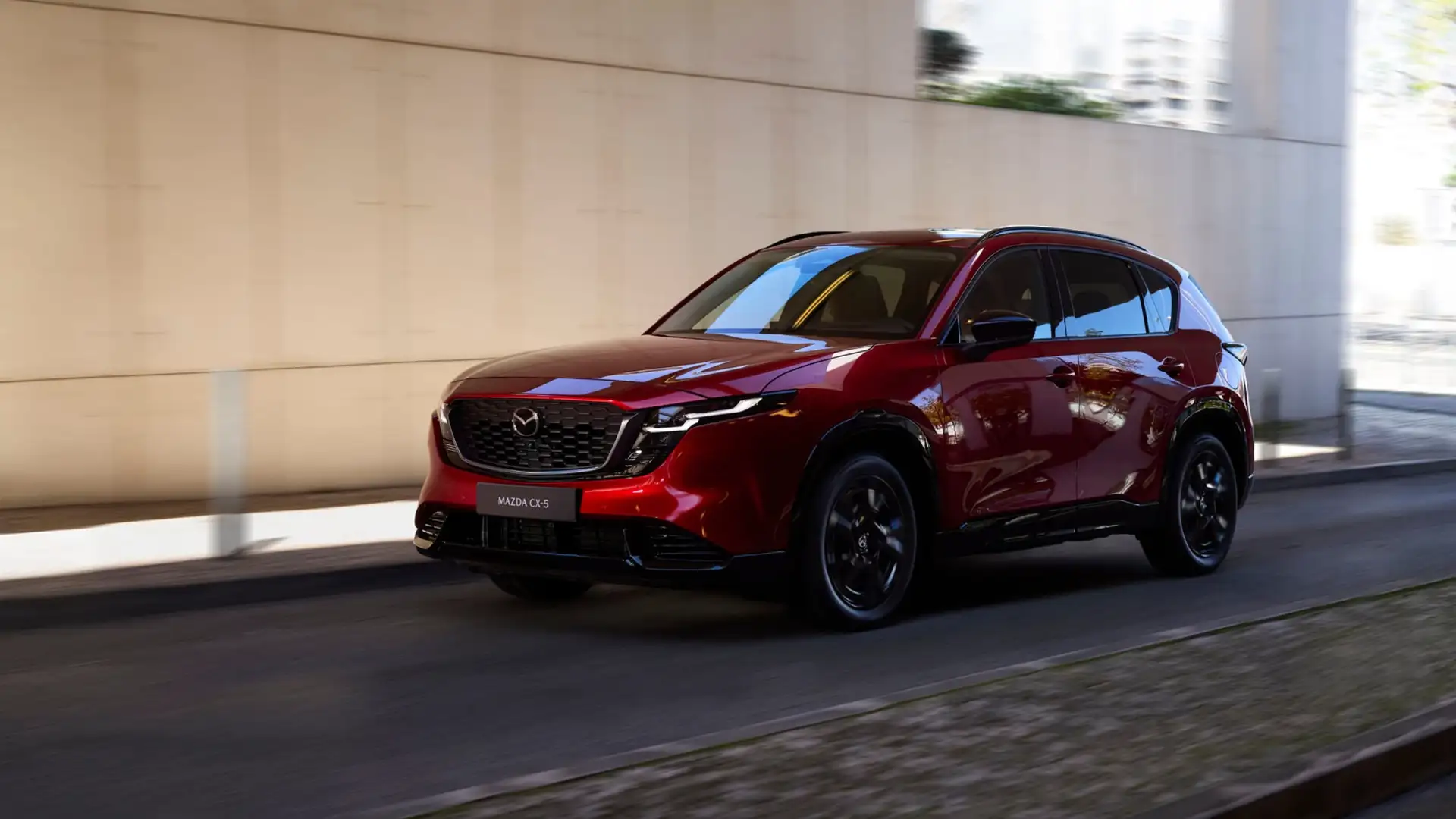 2026 Mazda CX-5 red SUV driving through an urban underpass with black wheels and roof rails