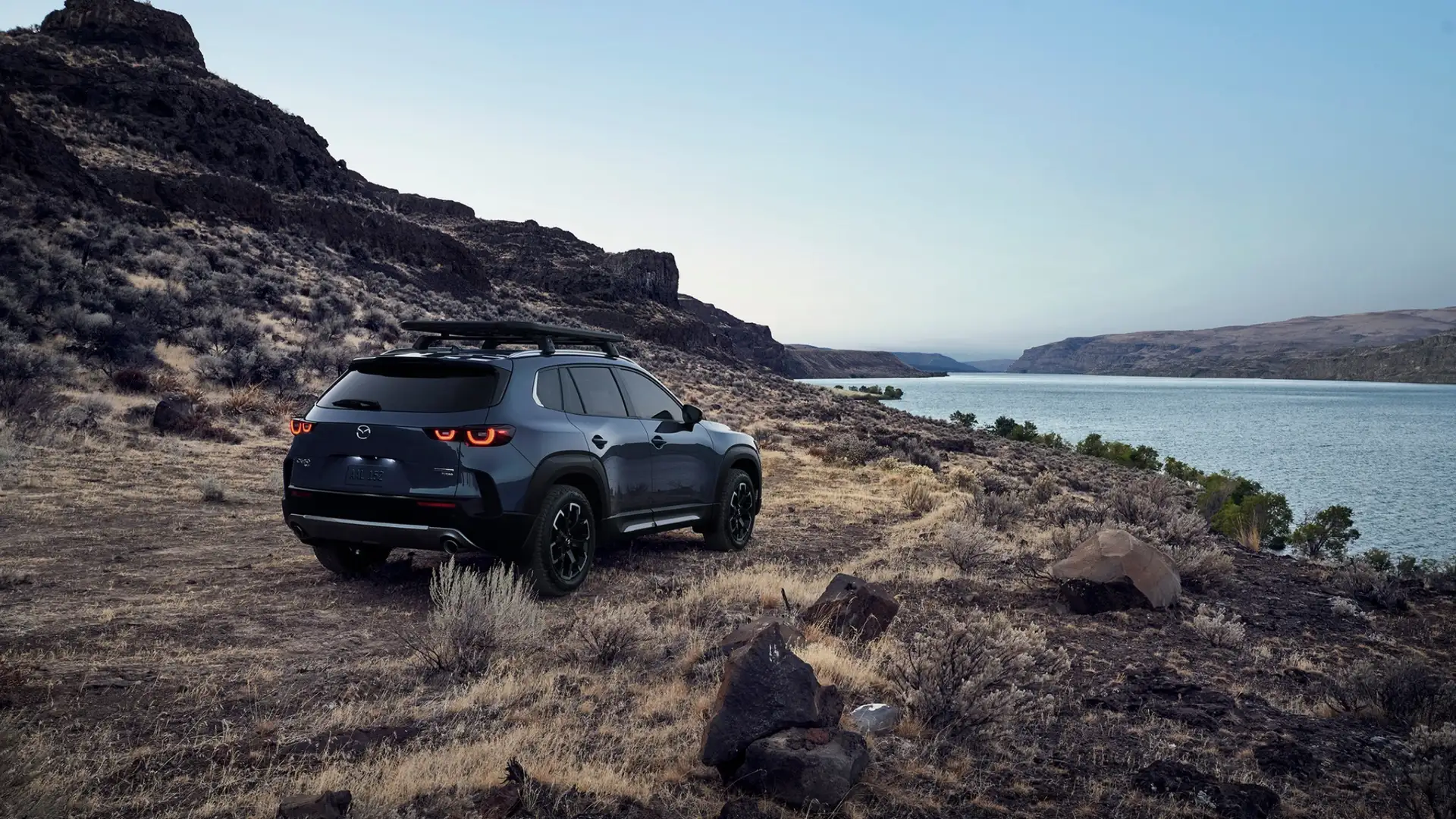 2026 Mazda CX-50 gray SUV parked on rocky canyon terrain overlooking a wide blue lake at dusk