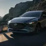 2026 Mazda3 Hatchback dark gray car driving on winding mountain road with rocky cliffs at sunset