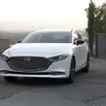 2026 Mazda3 Sedan white car parked on modern driveway with front grille and hillside view behind
