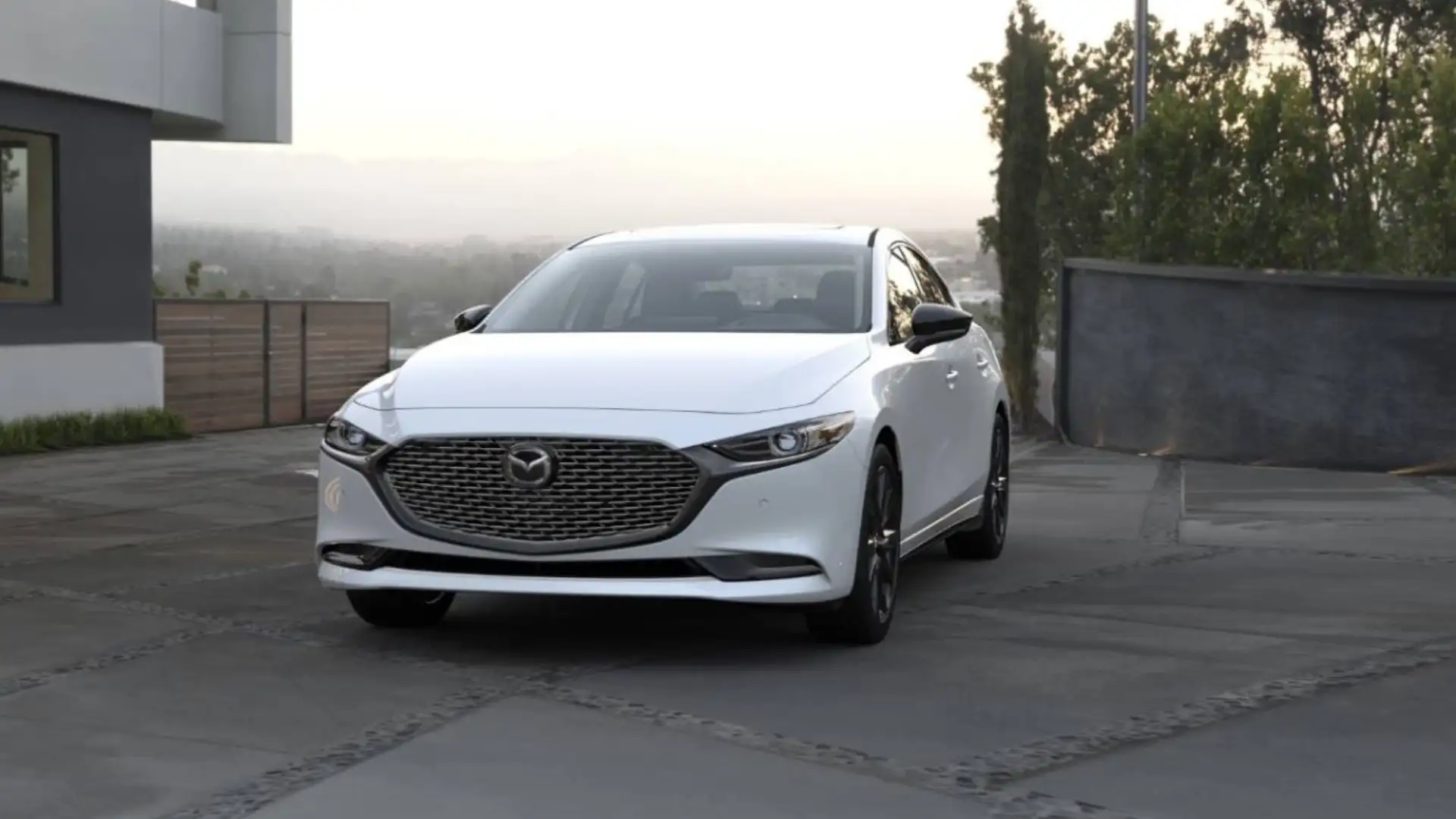 2026 Mazda3 Sedan white car parked on modern driveway with front grille and hillside view behind