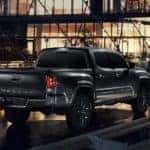 A black 2021 Toyota Tacoma is driving over a bridge at night, shown from the rear.