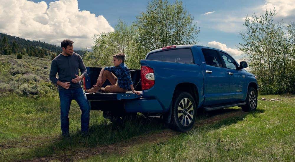 A man is talking to his son who is sitting on the tailgate of a blue 2021 Toyota Tundra that is parked on grass in Indiana, PA.
