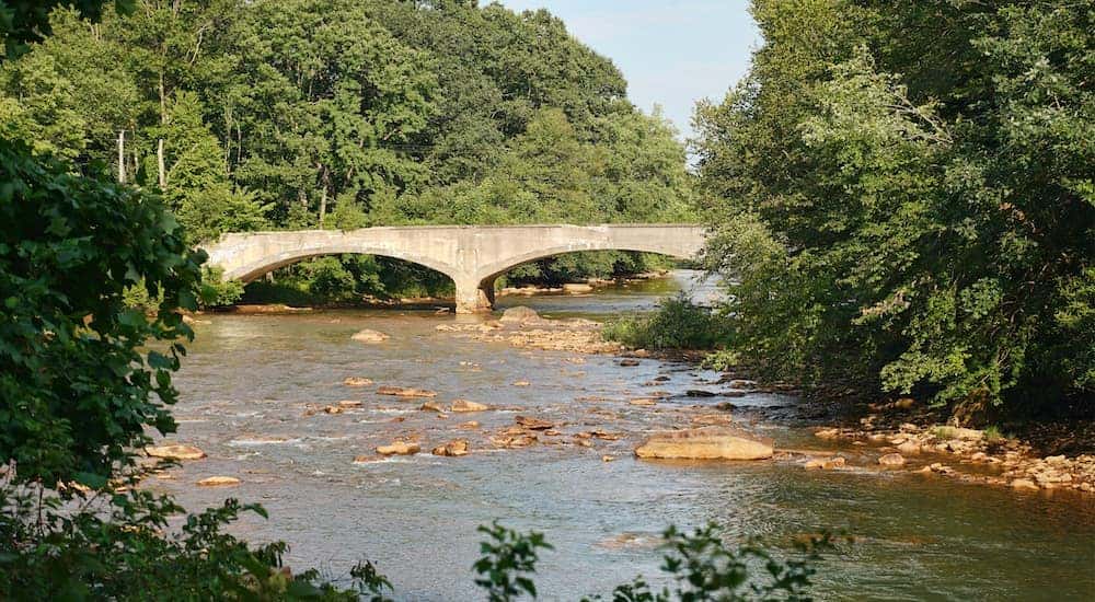 A bridge is shown over a river flanked by forrest.