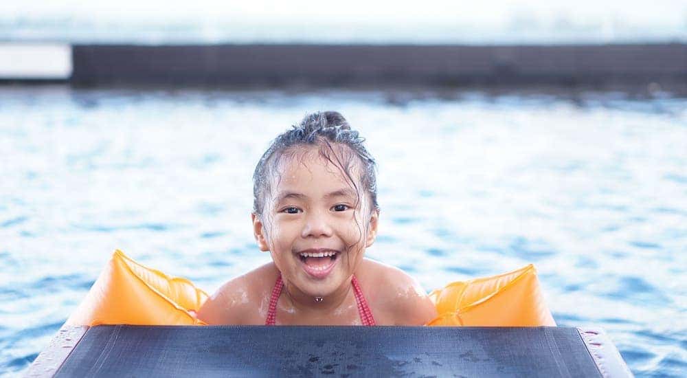 A smiling young girl with arm floats is in a pool.