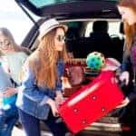 A group of teenage friends is shown unloading an SUV during a road trip.