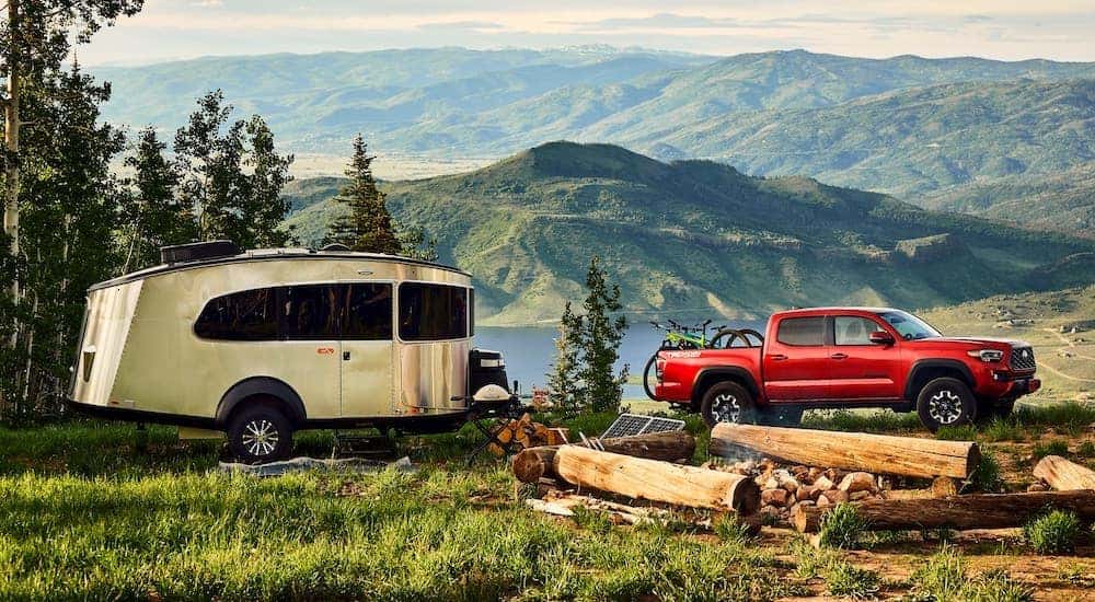 A red 2021 Toyota Tacoma TRD is shown from the side next to a trailer at a camp side by a lake.