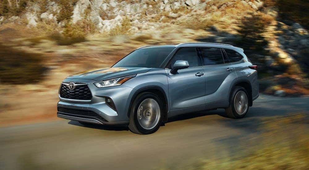 A blue 2020 Toyota Highlander is shown driving down a tree lined road after leaving a used Toyota dealership.