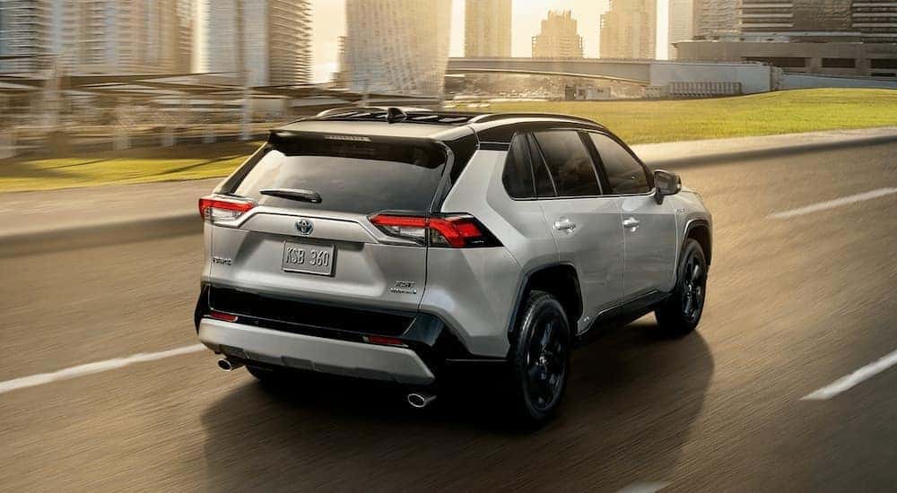 A silver 2020 Toyota RAV4 is driving past a city.
