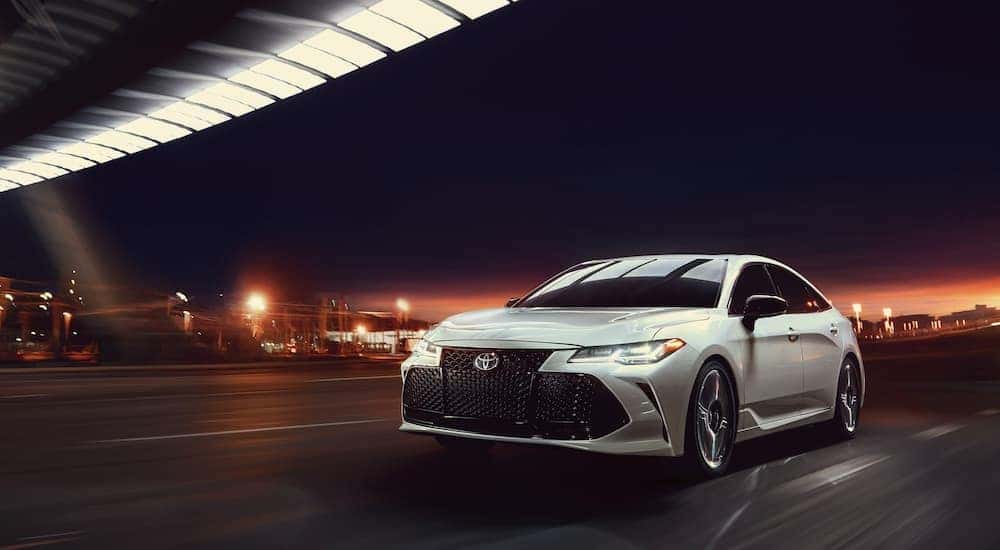 A reliable used Toyota for sale, a white 2020 Toyota Avalon, is shown driving under a bridge.