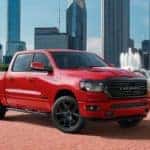 A red 2020 Ram 1500 is parked in front of a park with a city skyline in the distance.
