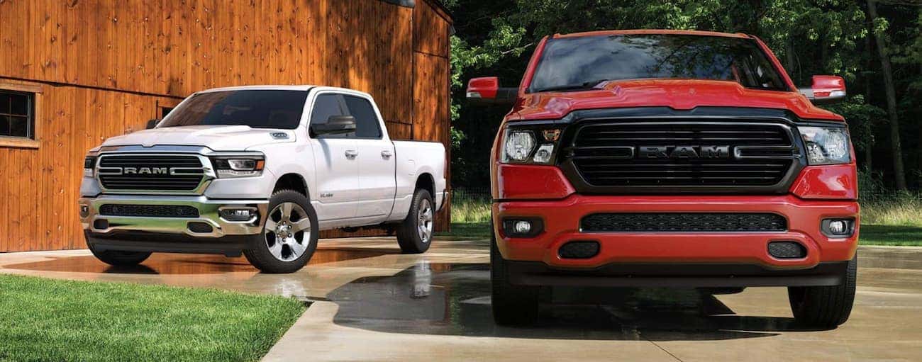 A red 2020 Ram 1500 is parked in front of a white one with a wooden barn behind them near Defiance, OH.