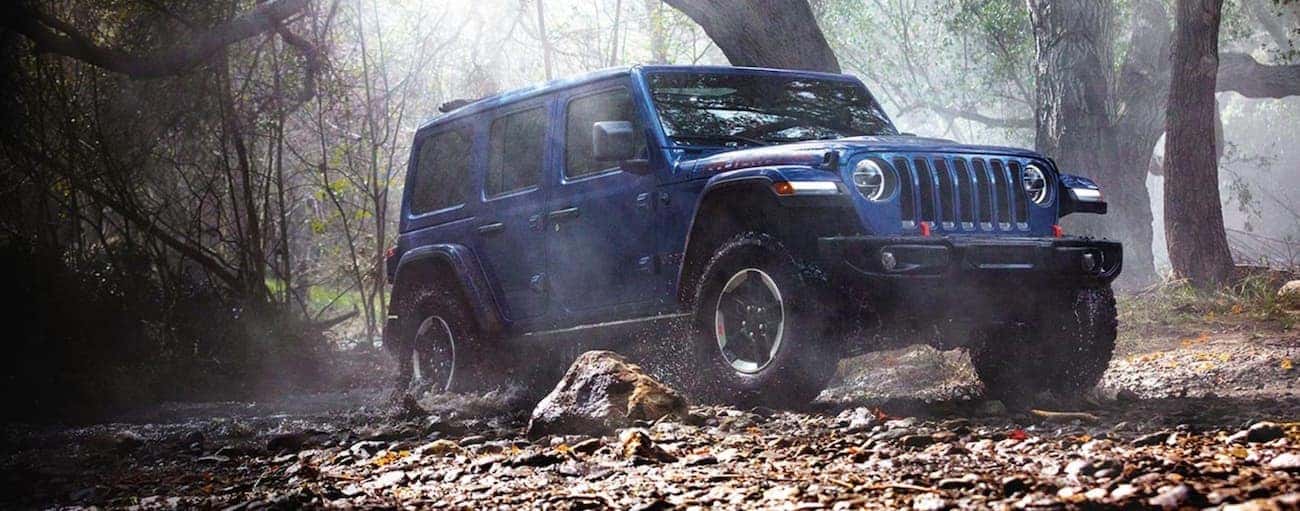 A blue 2020 Jeep Wrangler Unlimited is driving through the woods near Findlay, OH.