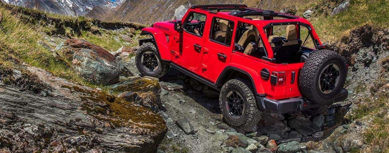 A red 2020 Jeep Wrangler Unlimited is off-roading on a rocky trail with the top off.
