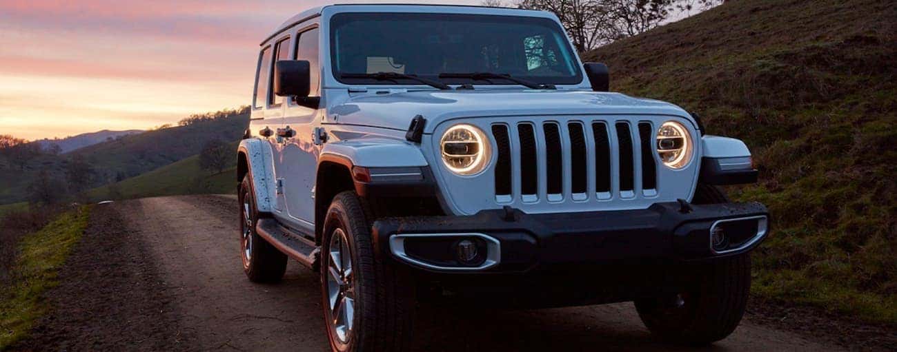 A white 2020 Jeep Wrangler Unlimited is driving with a sunset behind it.
