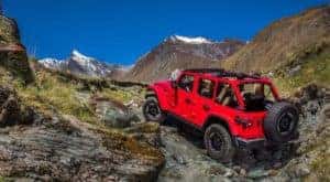 A red 2020 Jeep Wrangler Unlimited with no roof is climbing rocks on a mountain against a vibrant blue sky.