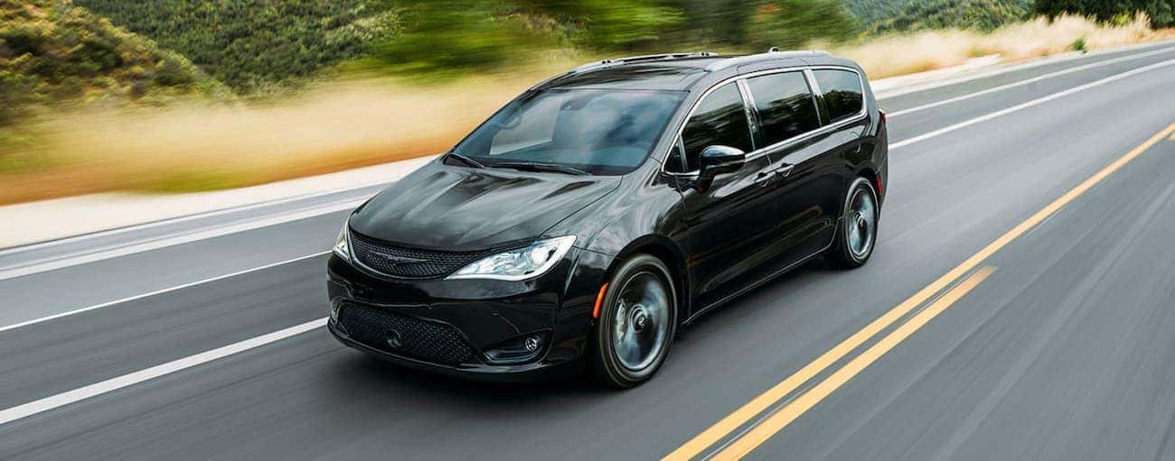 A black 2020 Chrysler Pacifica is driving on a road past blurred trees near Findlay, OH.