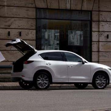 Man loading artwork into white 2022 Mazda CX-5 Compact Crossover SUV next to stone building