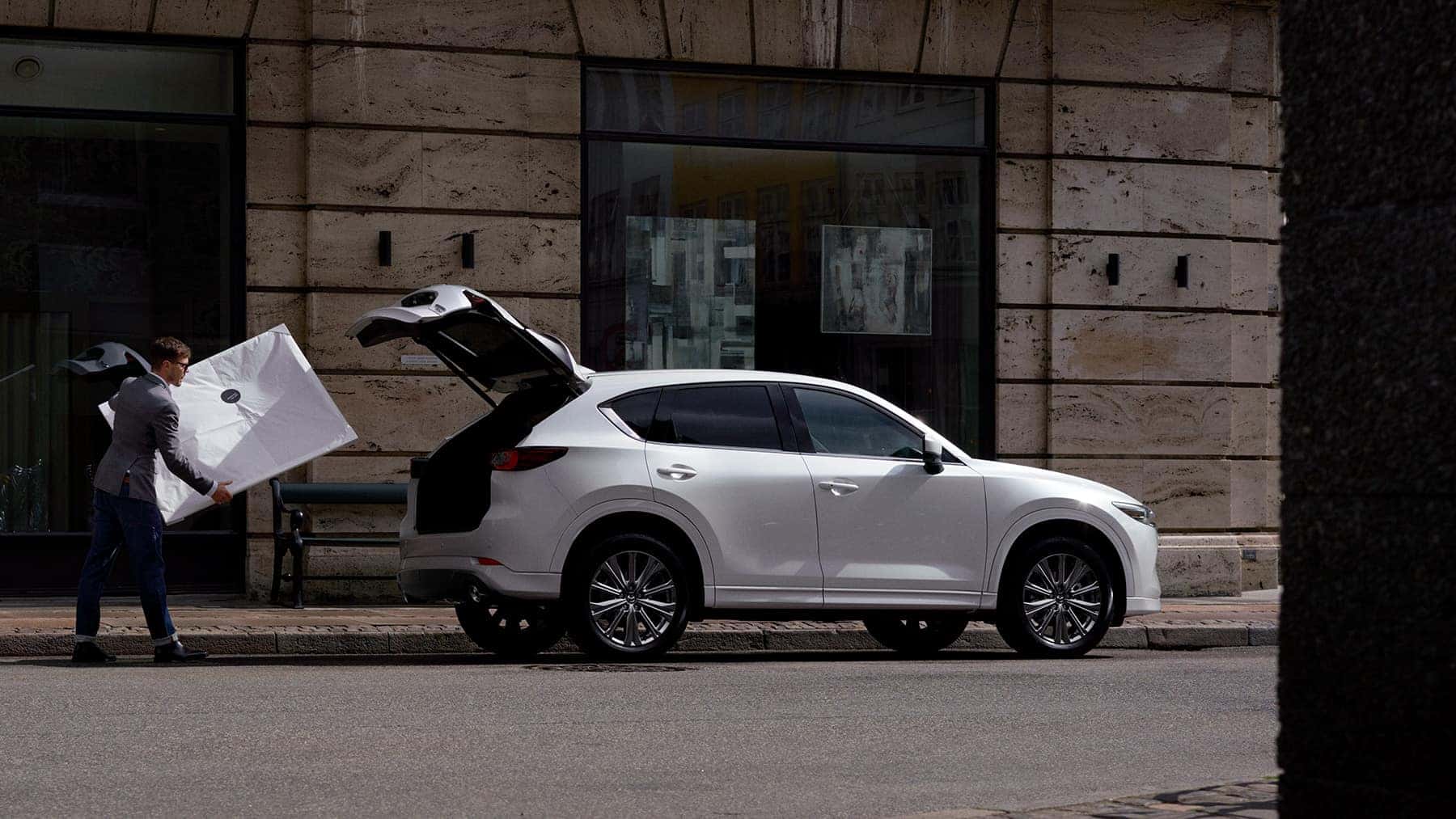Man loading artwork into white 2022 Mazda CX-5 Compact Crossover SUV next to stone building