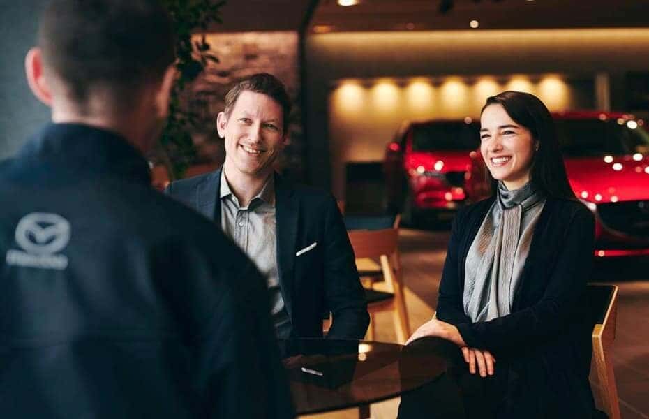 A man and a woman are having a conversation with a Mazda dealership employee