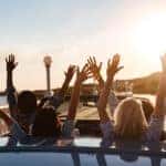 People holding hands out of convertible on road trip