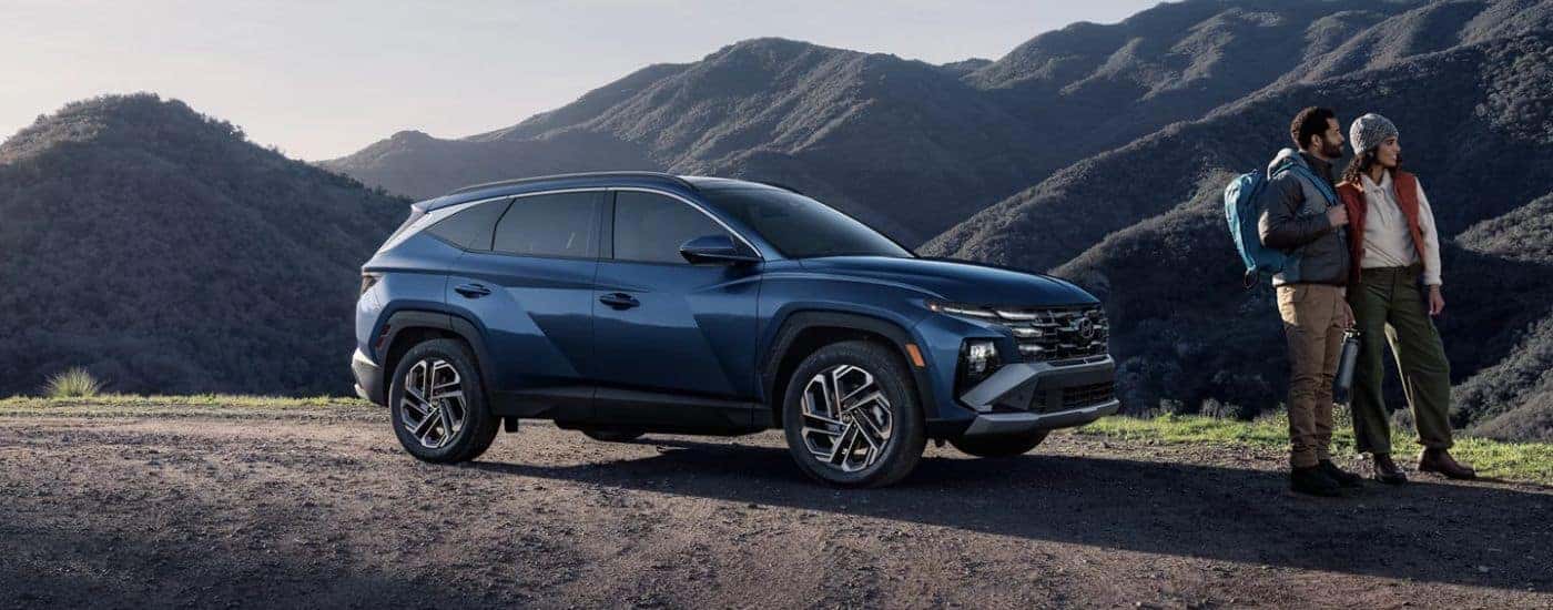 A blue 2026 Hyundai Tuscon Limited shown parked by two hikers and mountains.