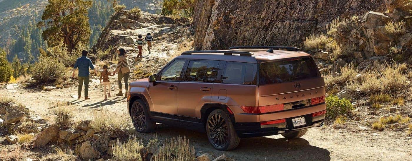 Brown 2026 Hyundai Santa Fe parked near a trail with a family walking away.