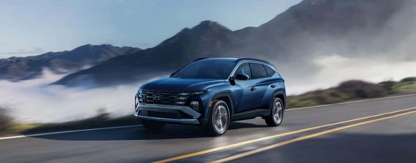 A blue 2026 Hyundai Tuscon Limited shown driving a foggy mountain-lined road.