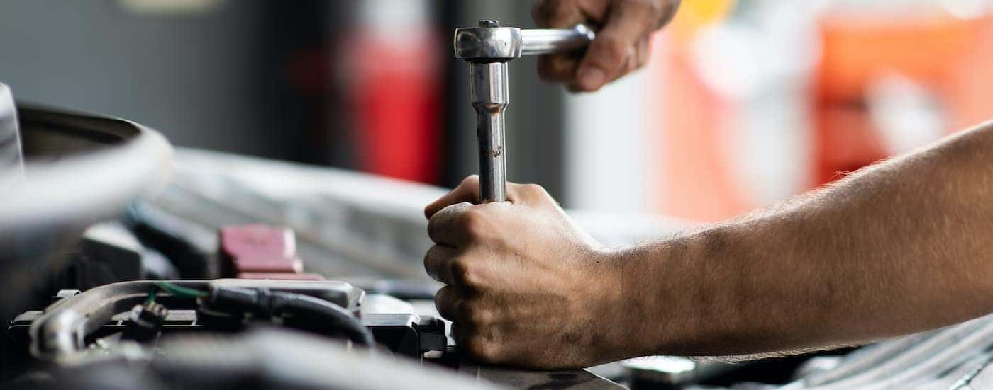 A mechanic using a socket wrench under the hood of a vehicle