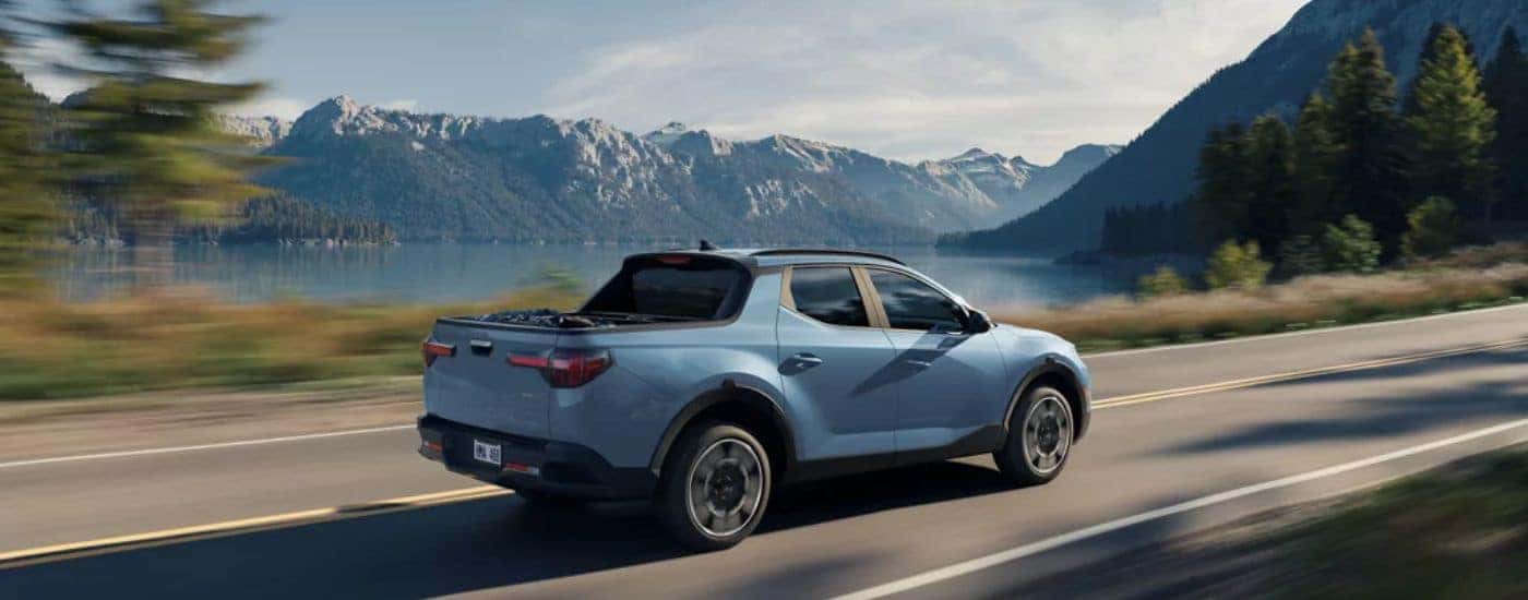 Blue 2026 Hyundai Santa Cruz driving on a paved road near the mountains.