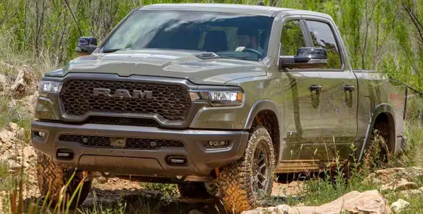 Olive green RAM 1500 with a lifted suspension wading through tall grass and shallow water