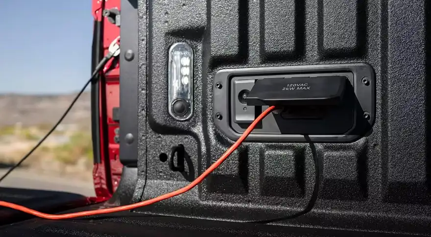 Power cord plugged into the 115-volt outlet inside the bed of a red RAM 1500