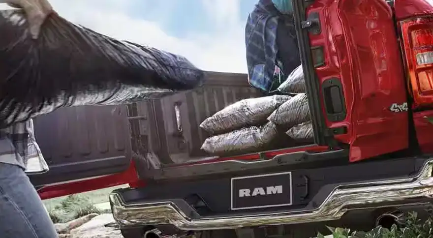 Two people loading firewood into a red RAM 1500 through the open swing-away multifunction tailgate