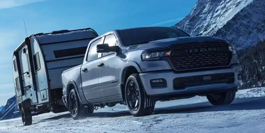 Silver RAM 1500 backing up to a camper trailer on packed snow with mountains behind