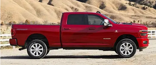 Red RAM heavy-duty crew cab pickup parked beside a wooden fence in front of desert hills